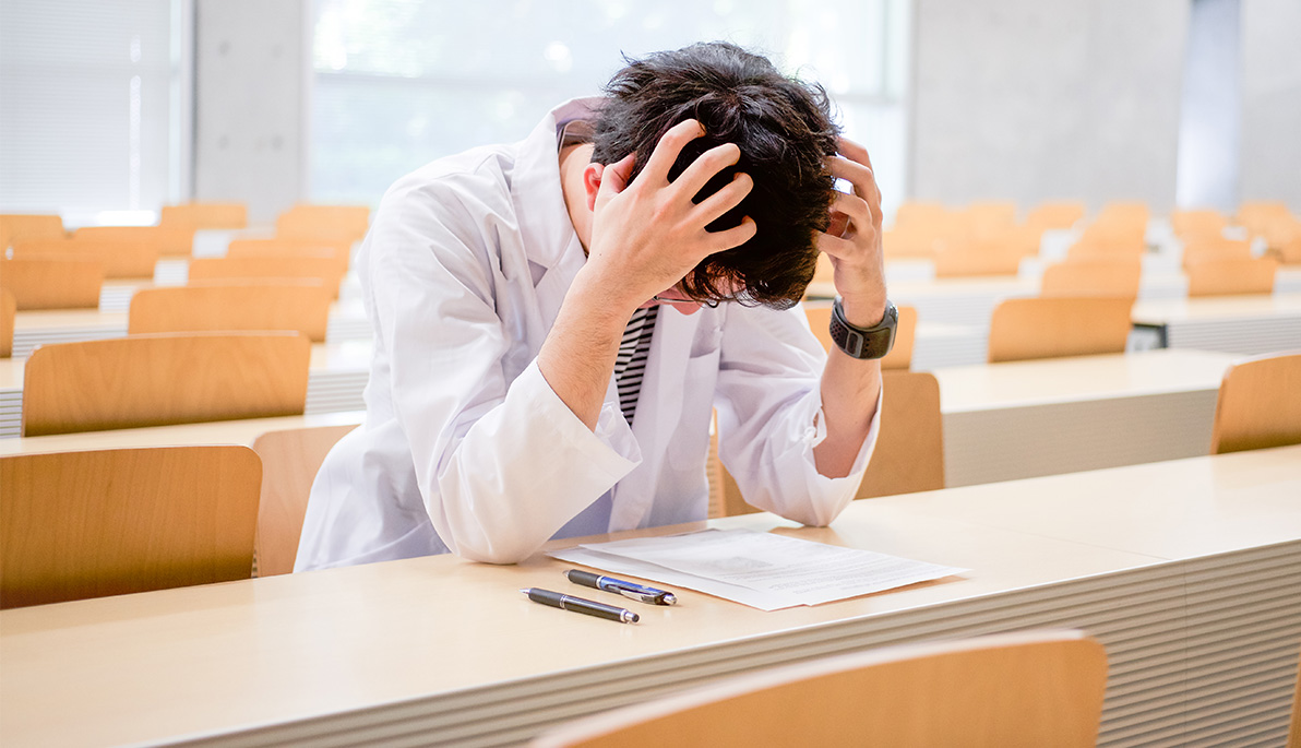 Physician in white coat sitting with hands on head