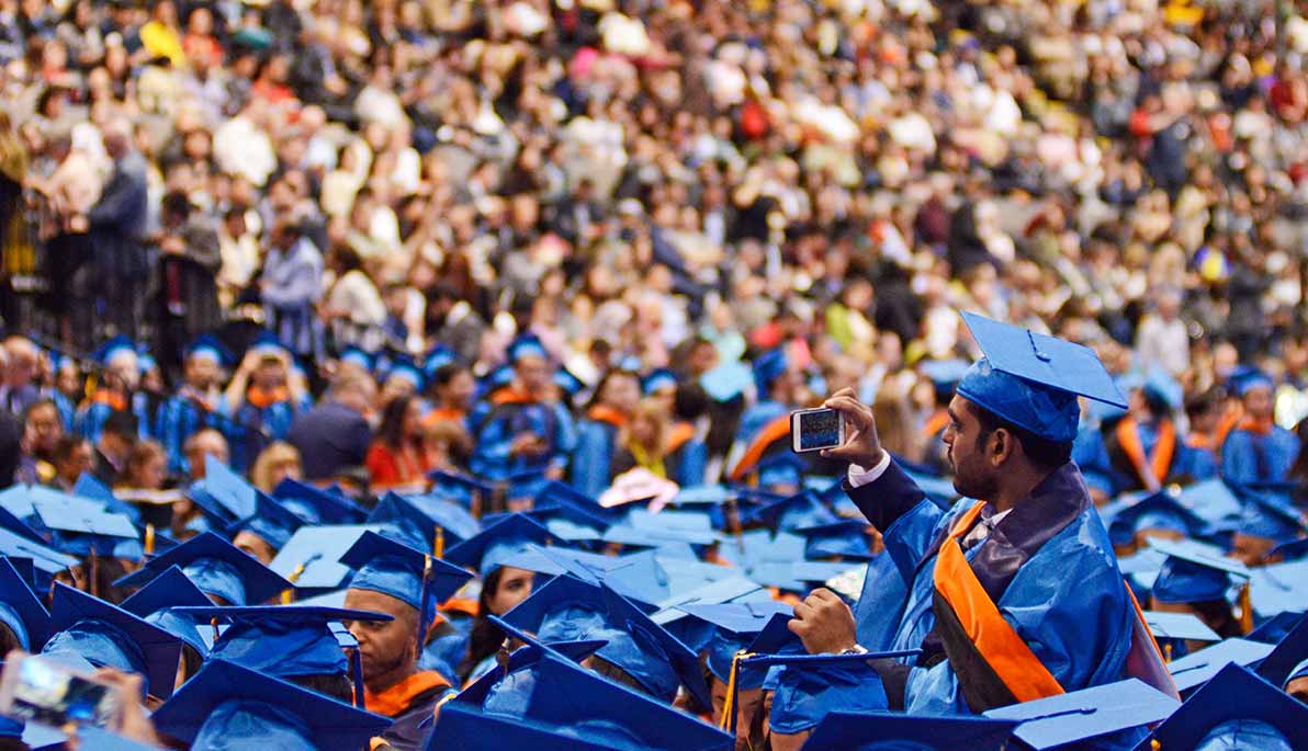 Student taking photo with camera in a sea of graduates at NYIT Commencement 2018