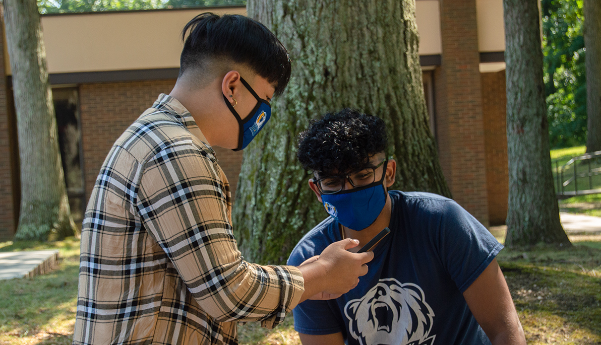 Two students wearing masks looking at phone.