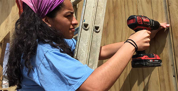 Woman on a ladder using a drill on a wall