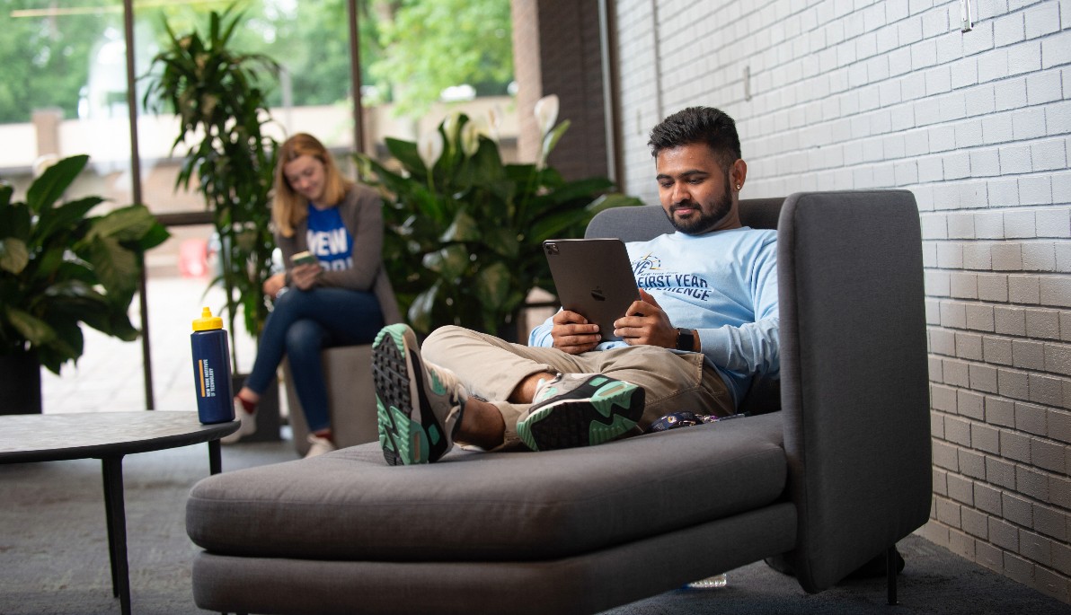 Man sitting in a lounge chair looking at a tablet.