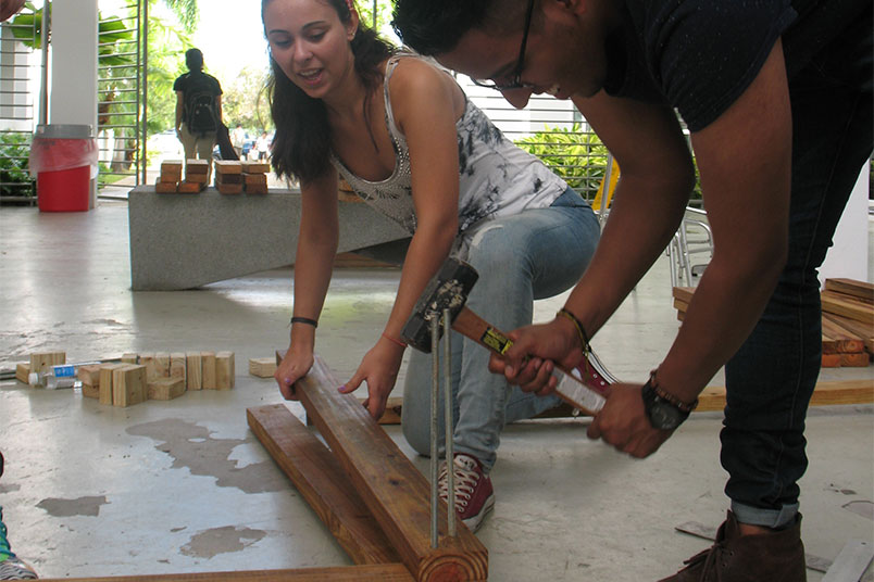 NYIT architecture student Jorge Villao hammers metal rods into a wooden beam.