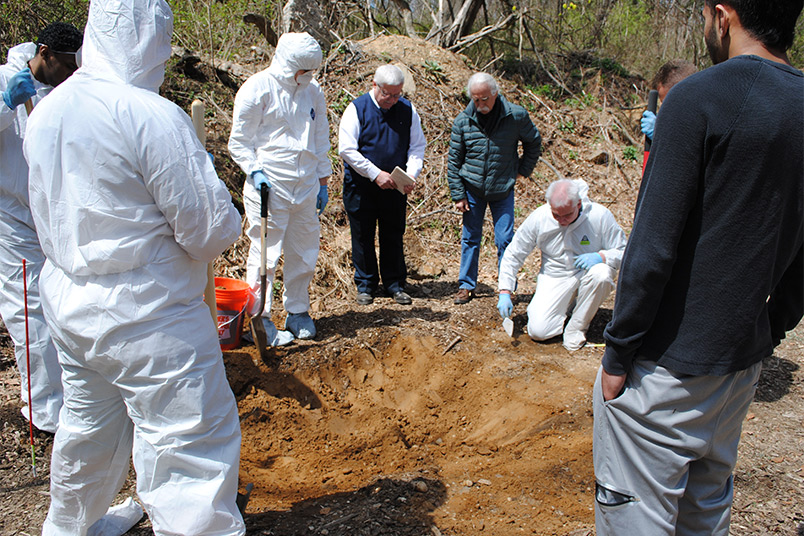 Carefully digging through the dirt to find the buried body.