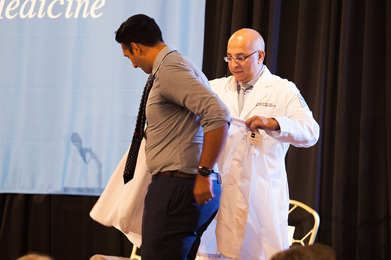 Keynote speaker Atul Kukar, D.O., coats a student.